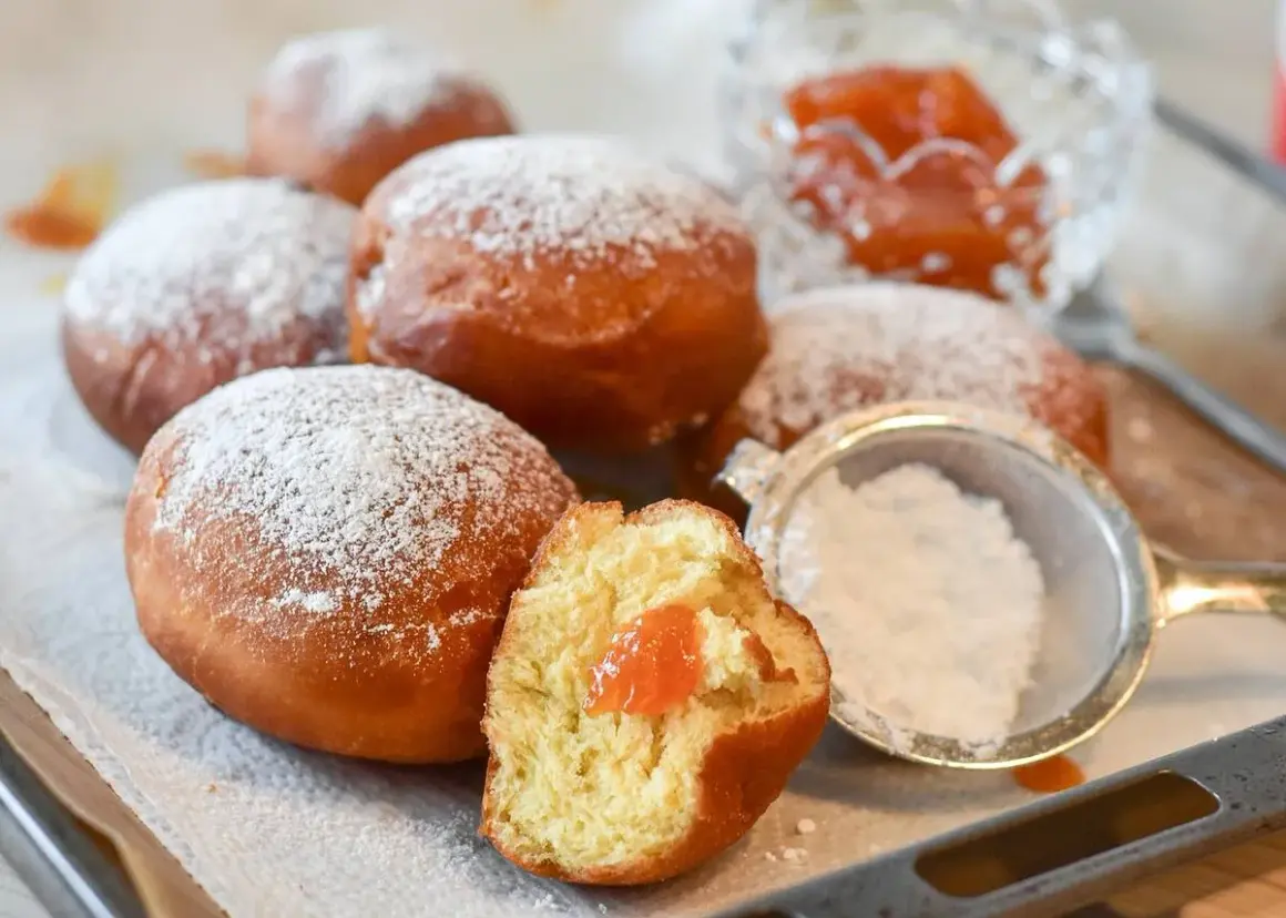 Rosquillas de naranja recién hechas, espolvoreadas con azúcar glas. Una está partida, mostrando su relleno de mermelada.