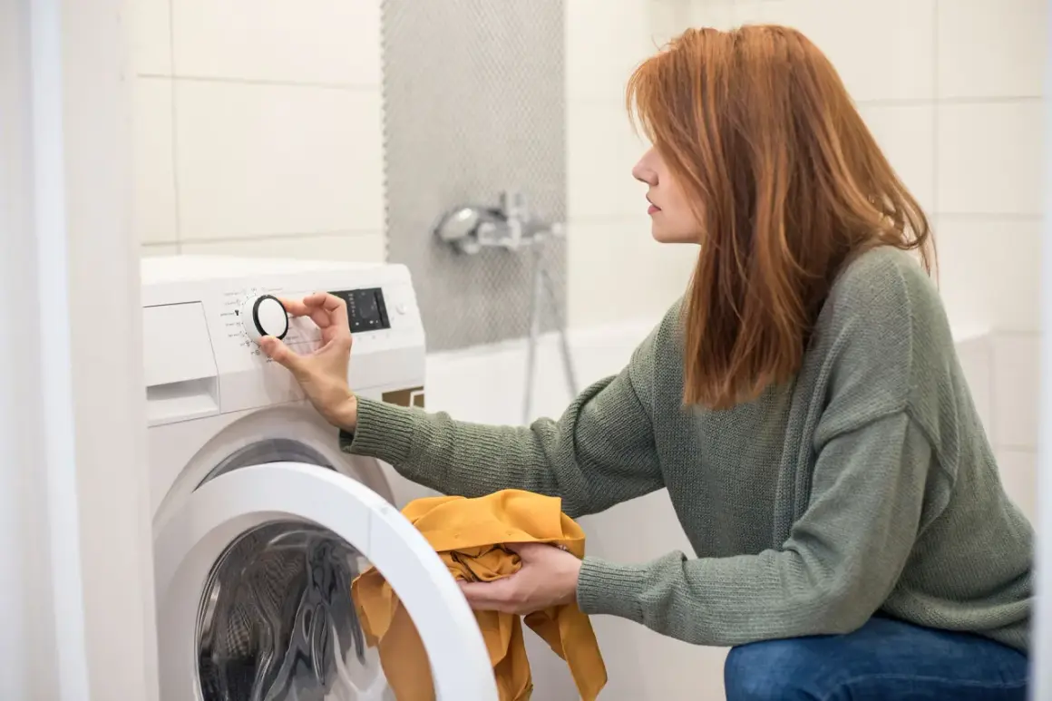 Frau stellt Waschmaschine ein, um den Wasserverbrauch zu optimieren. Sie hält ein gelbes Kleidungsstück in der Hand.