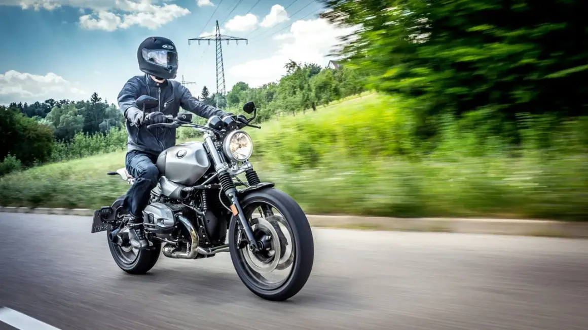 Motocyklista w kasku i kurtce jedzie drogą. Kask i kurtka to obowiązkowe wyposażenie motocykla, zapewniające bezpieczeństwo.