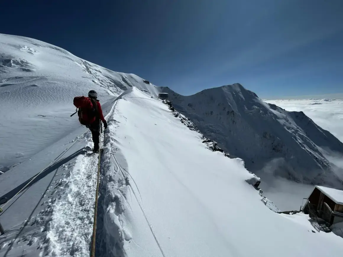 Bergsteiger auf dem Weg zum Mont Blanc besteigen, gesichert durch ein Seil, mit atemberaubendem Blick auf schneebedeckte Gipfel und Wolkenmeer.