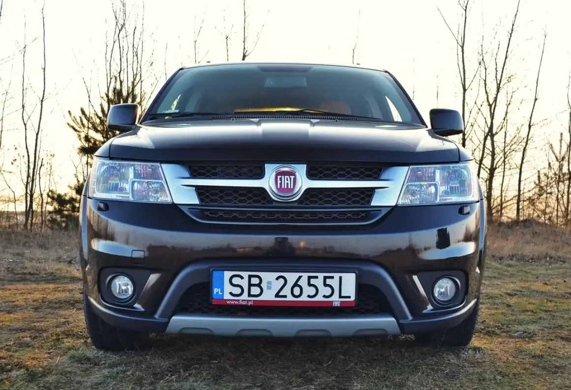 Czarny Fiat Freemont na tle drzew. Zastanawiasz się nad jego spalaniem? Ten SUV oferuje przestronne wnętrze i komfort podróżowania.