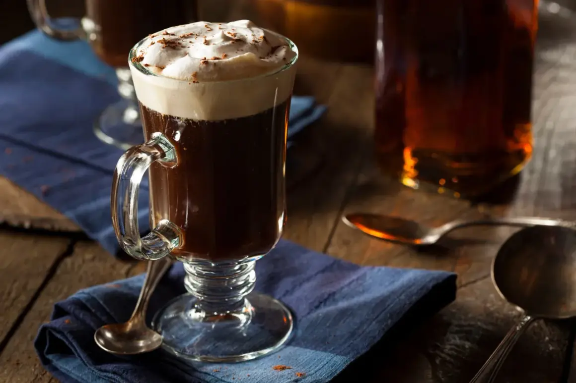 En värmande irish coffee med vispad grädde och kanel på en blå duk.