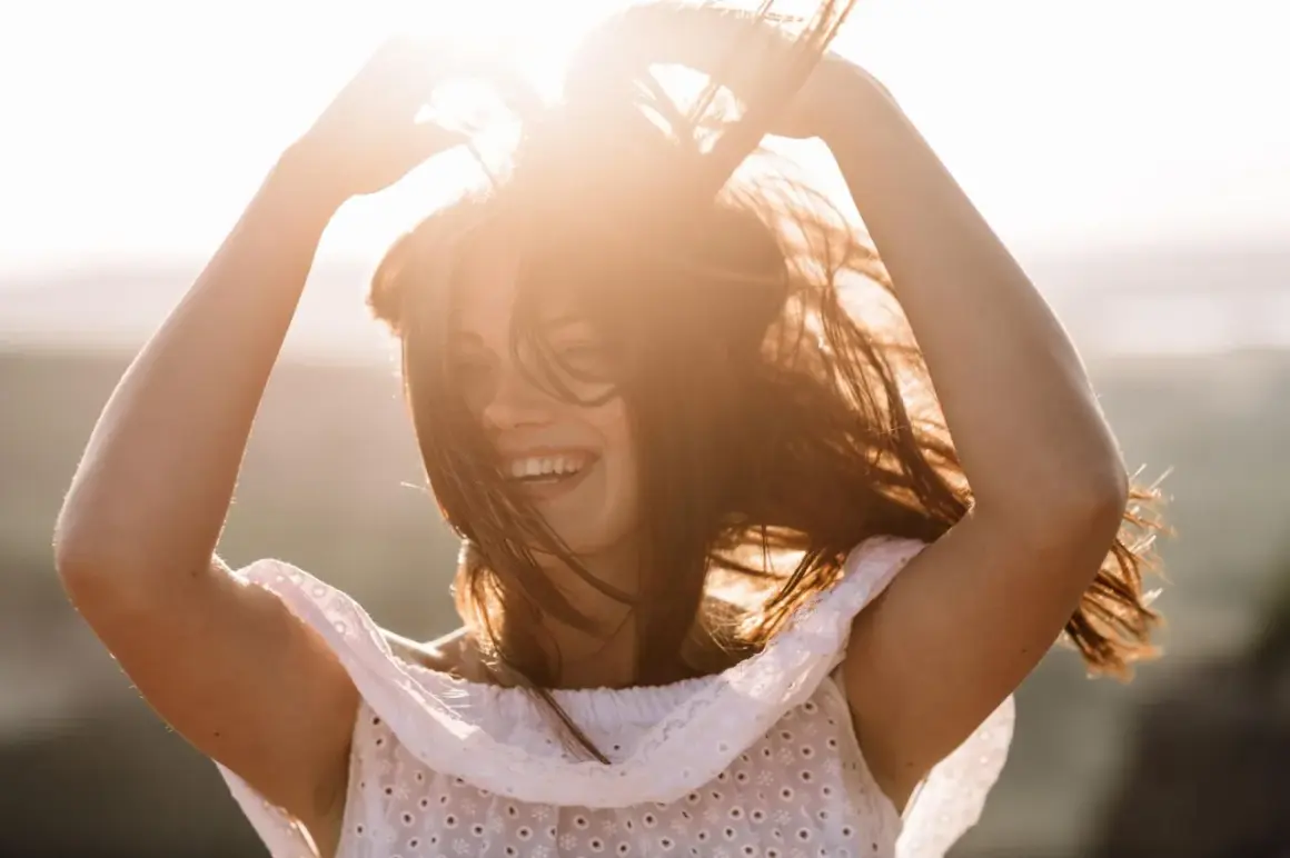 Lachende Frau mit fliegenden Haaren im Sonnenlicht. Ein Gefühl von Freiheit, das auch in den Wechseljahren möglich ist.