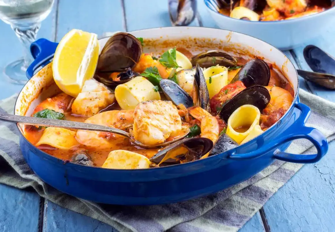 Caldereta de pescado humeante en cazuela azul, con gambas, mejillones, trozos de pescado blanco y limón.