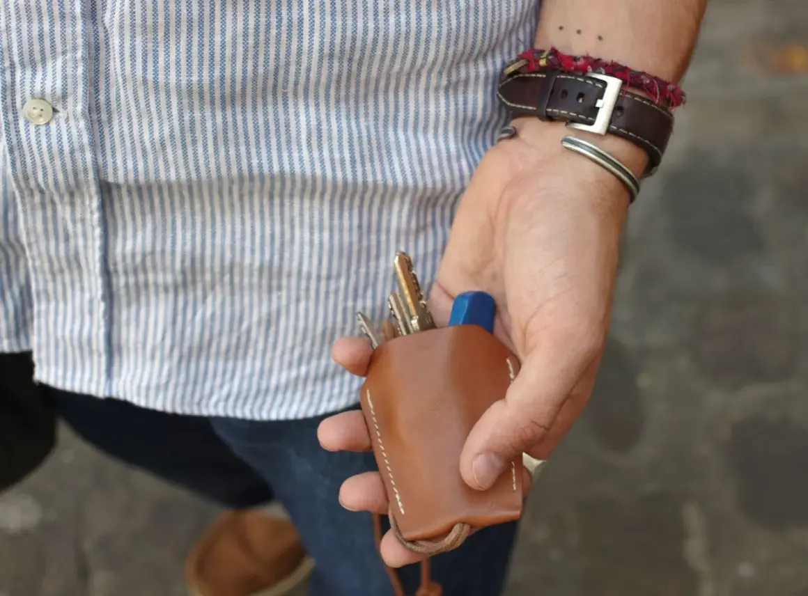 Main d'un homme au style workwear, tenant un étui à clés en cuir marron.