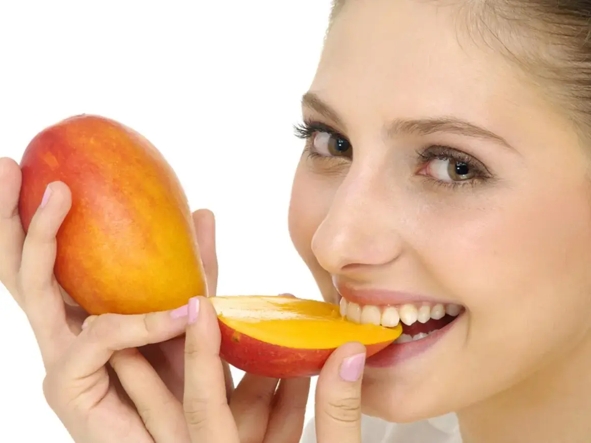 Ragazza sorridente morde un mango succoso, sapendo che il mango è lassativo.