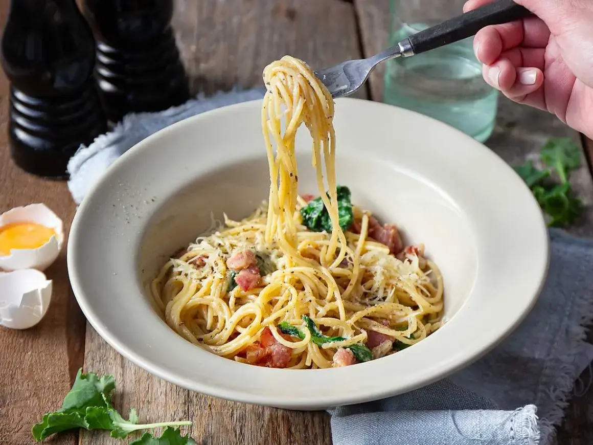 En gaffel lyfter en portion krämig spaghetti carbonara från en skål. Ett perfekt pasta carbonara recept för en god middag.