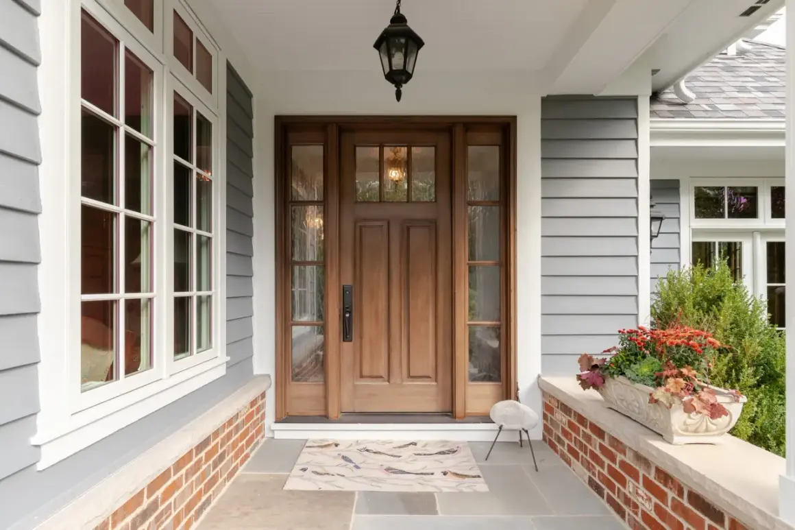 A beautiful front door makeover featuring a warm wooden door with glass panels, flanked by windows. A bird-themed doormat welcomes guests.