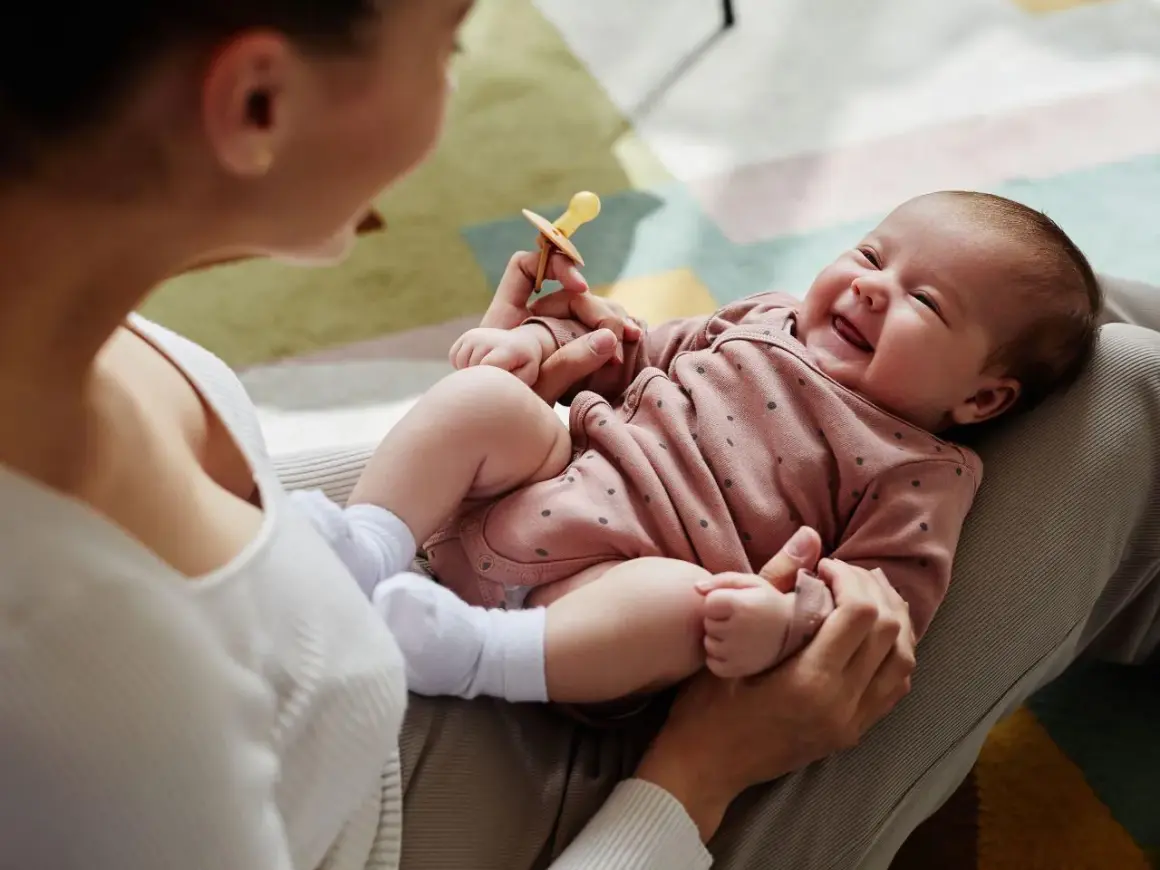 Mama bawi się z dzieckiem, które radośnie gaworzy, trzymając smoczek.