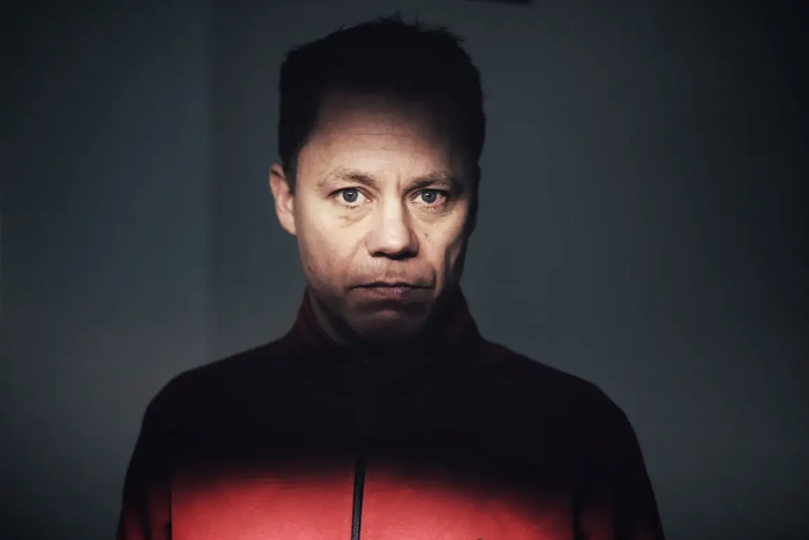Knut Koivisto, en man med intensiv blick, bär en röd jacka. Ljuset faller dramatiskt över hans ansikte.