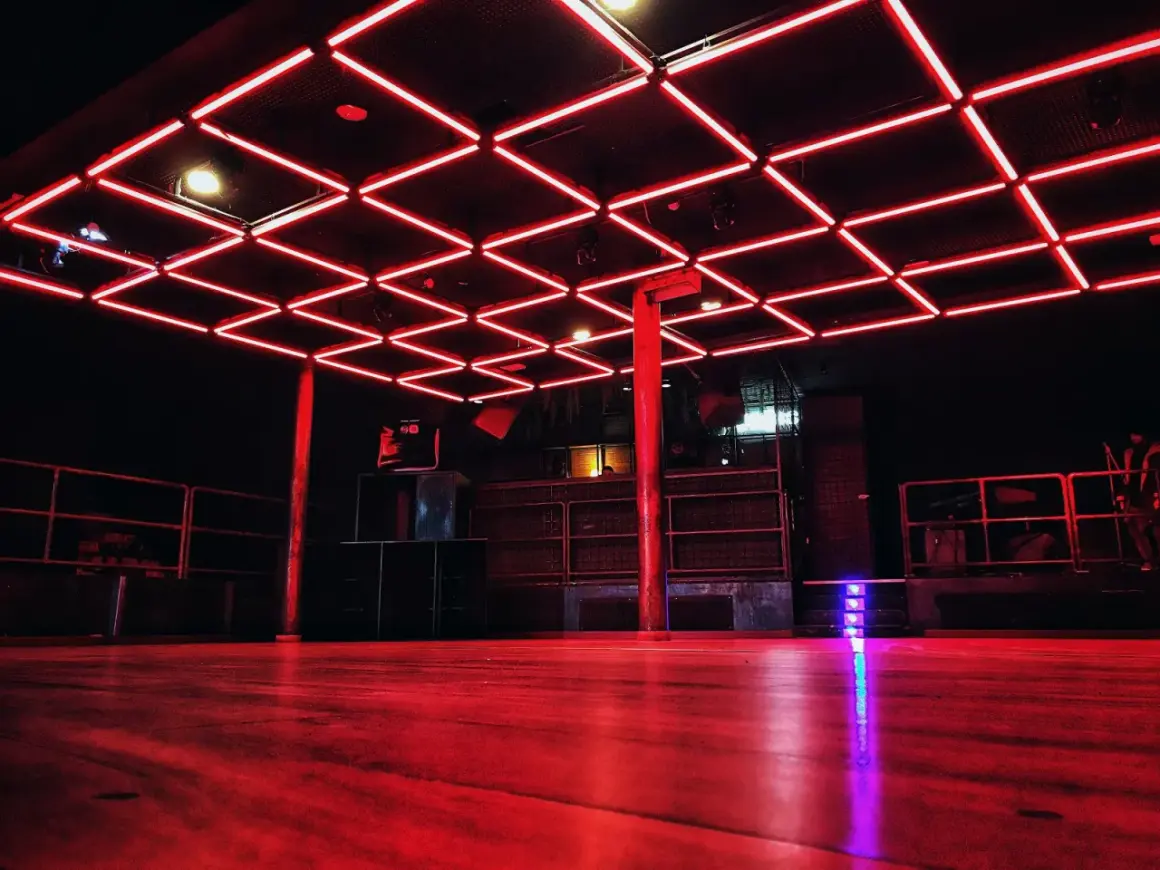 Interno di un basic club con luci al neon rosse sul soffitto e pavimento in legno.