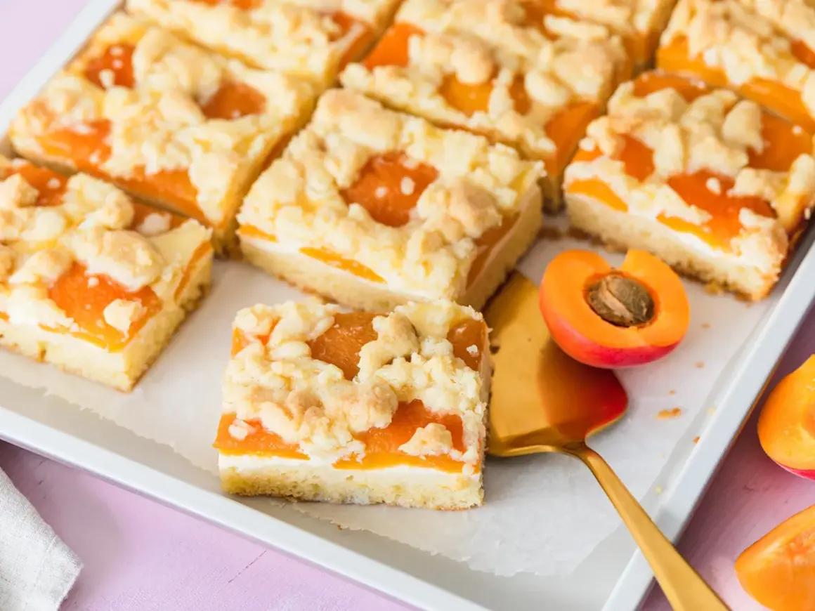 Saftiger aprikosenkuchen mit buttrigen streuseln, perfekt für den Sommer. Ein Stück ist mit einem goldenen Kuchenheber herausgenommen.