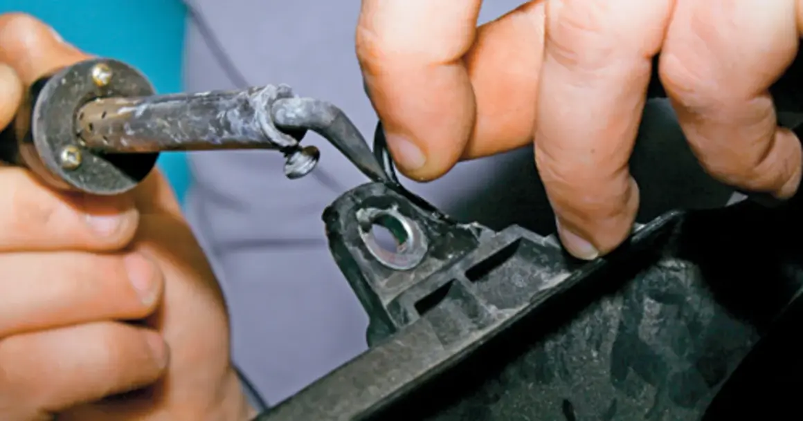 Ręce trzymają lutownicę i plastikowy element, pokazując jak skleić plastik bez kleju, topiąc go.