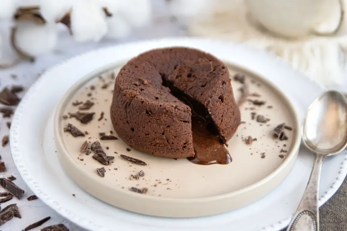 Ein warmes Schoko Soufflé mit flüssigem Kern, garniert mit Schokostückchen auf einem Teller.