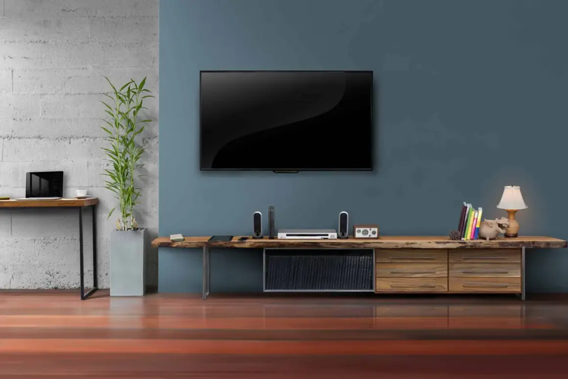 Moderner fernseher im wohnzimmer, daneben ein schlichtes Sideboard mit Deko und Büchern.