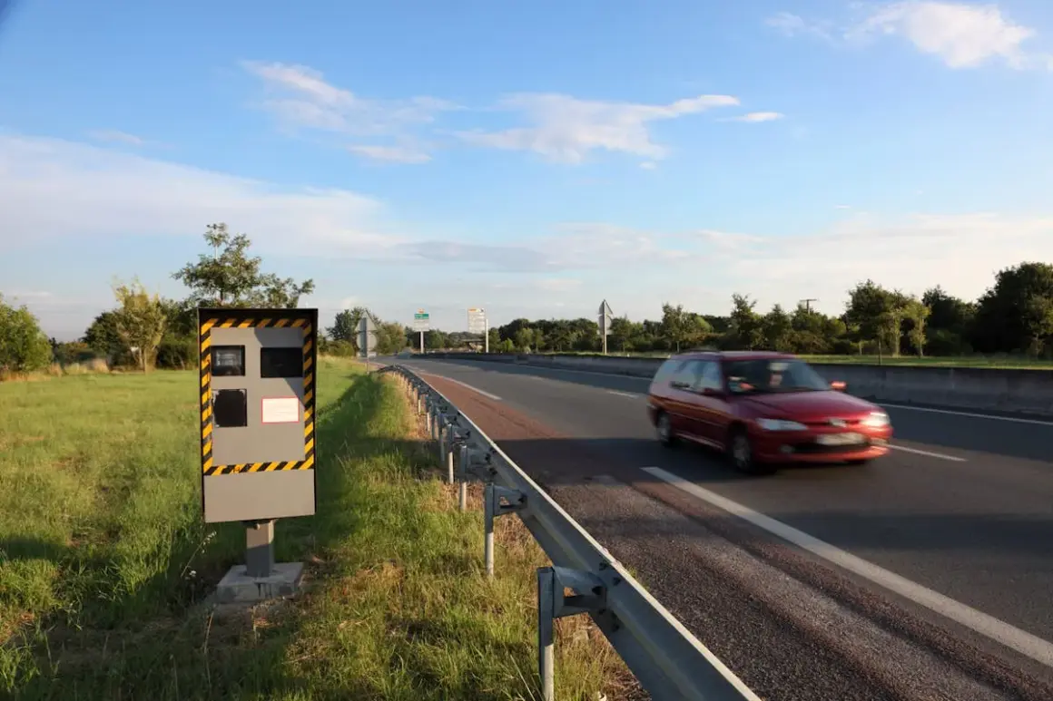 Un radar de chantier surveille la route. Une voiture rouge passe vite.