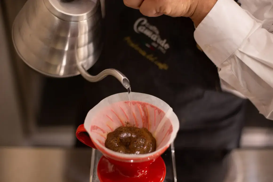 Versando acqua calda su caffè macinato in un filtro di carta rosso, per preparare un caffè filtro. Ecco come funziona la caffettiera americana.