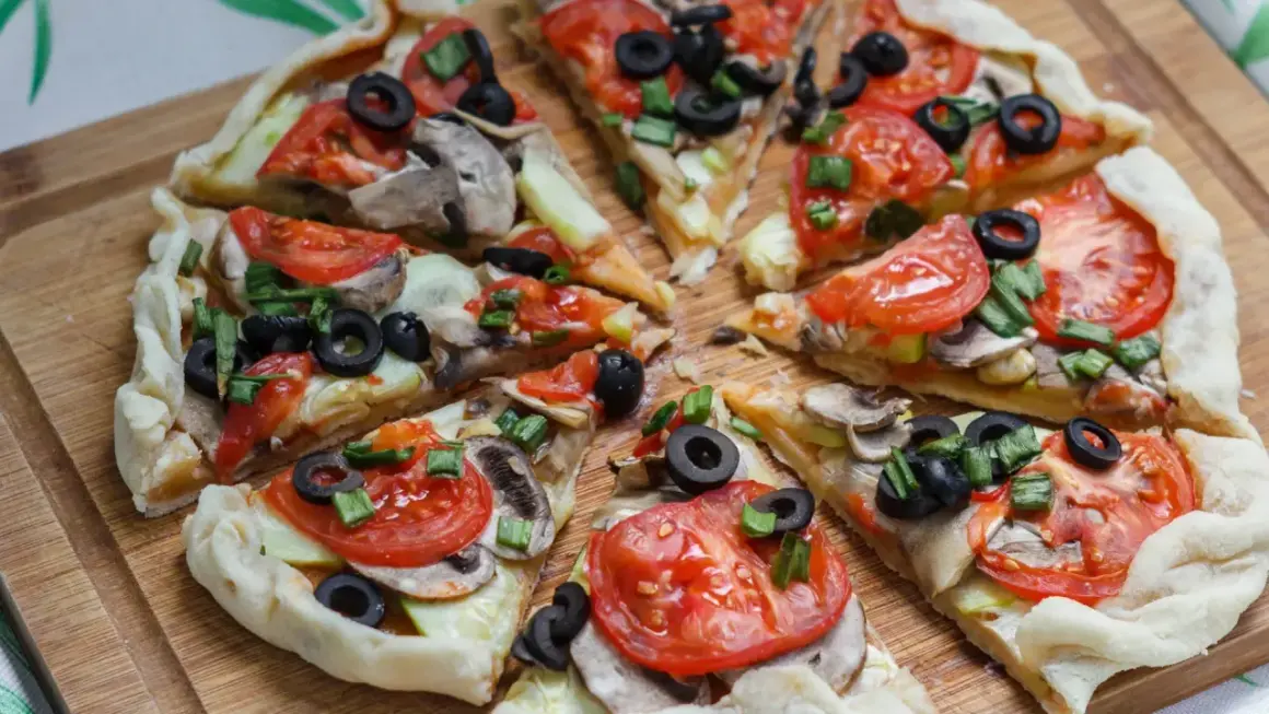 Kawałki pysznej, **zdrowej pizzy** z pomidorami, oliwkami i pieczarkami na drewnianej desce.
