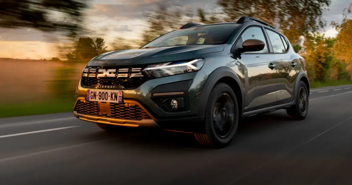 Zielony Dacia Sandero Stepway pędzi po drodze o zachodzie słońca, otoczony rozmazanymi drzewami i mglistym krajobrazem.