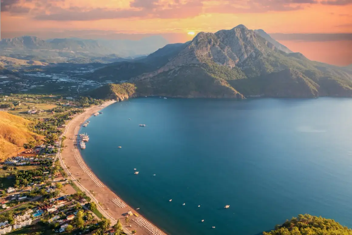 Widok z lotu ptaka na wybrzeże Turcji. Piękne turkusowe morze, piaszczysta plaża z leżakami i góry w tle o zachodzie słońca.