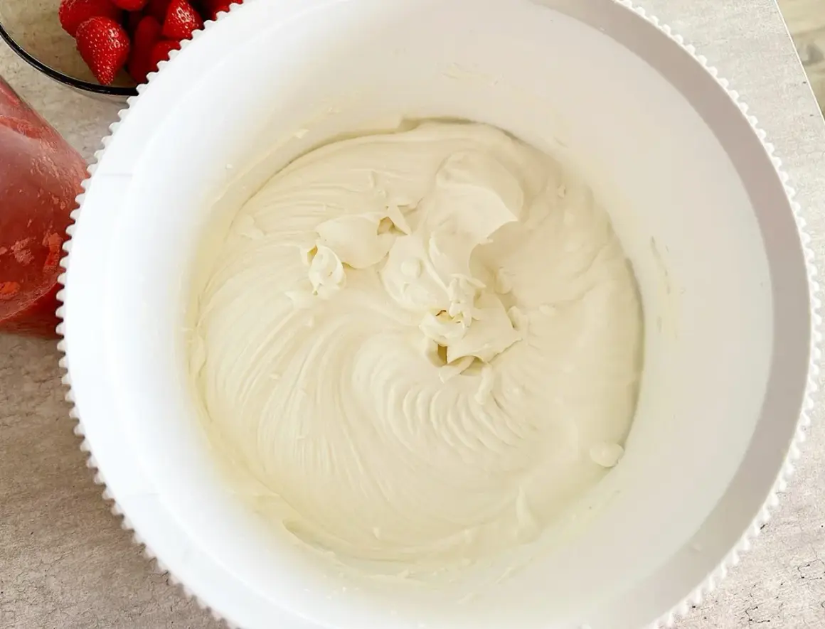 Gładka, kremowa masa z mascarpone w białej misie, gotowa do deseru. Obok widać miseczkę z truskawkami.