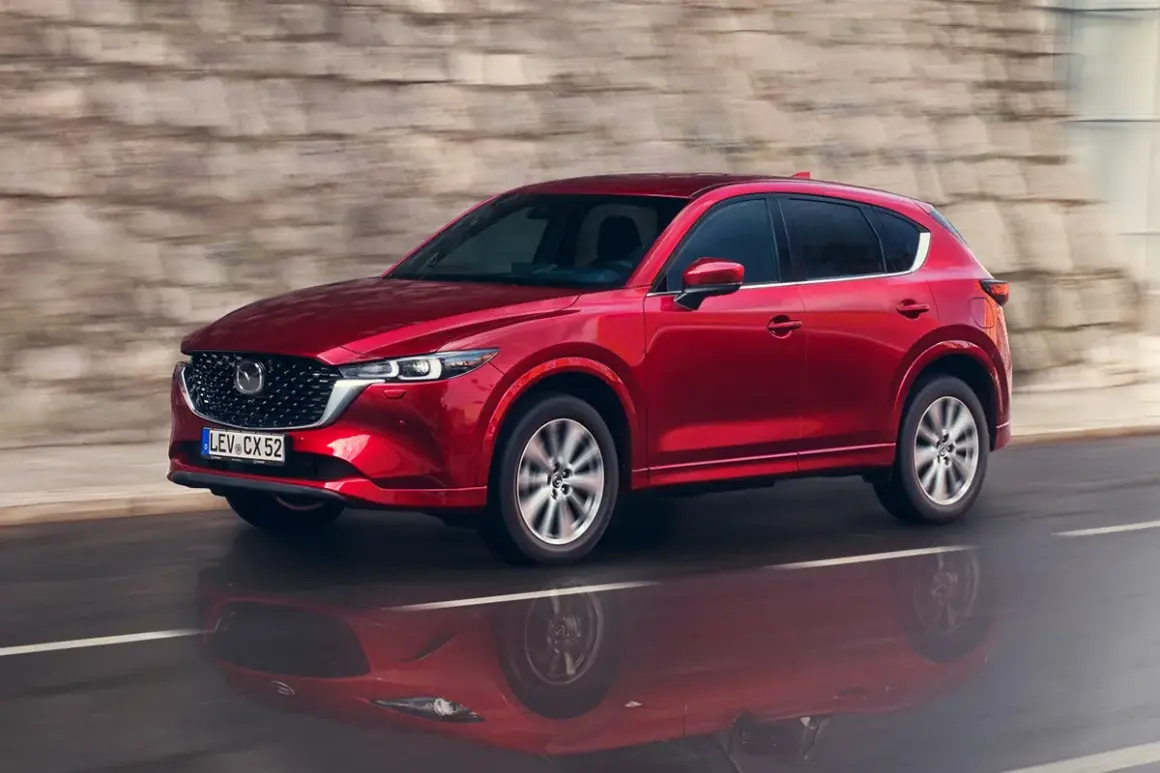 Czerwony suv Mazda CX-5 jedzie po mokrej drodze, odbijając się w kałuży.