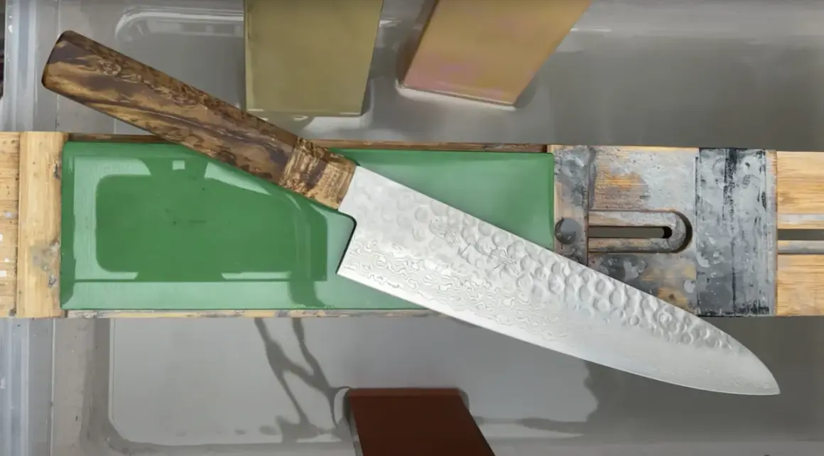 Ein japanisches Messer mit Damastmuster wird auf einem Schleifstein mit präzisem Schleifwinkel geschärft.