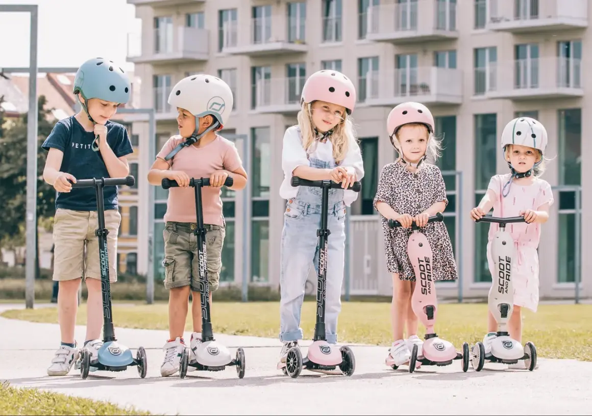 Fizjoterapeuta poleca Scoot and Ride dla dzieci. Pięcioro maluchów w kaskach na hulajnogach, gotowych do zabawy.