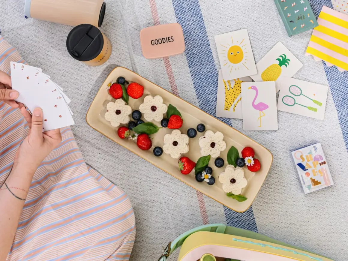 Picnic per bambini con panini a forma di fiore, fragole, mirtilli e carte da gioco colorate.