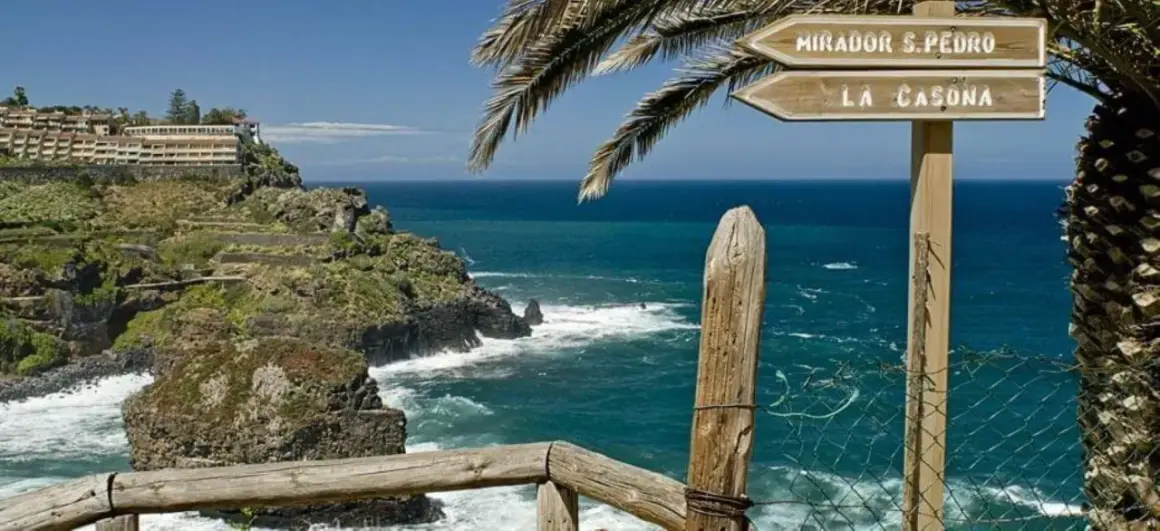 Cartel indicador en el sendero rambla de castro, señalizando Mirador S. Pedro y La Casona, con el mar azul de fondo.