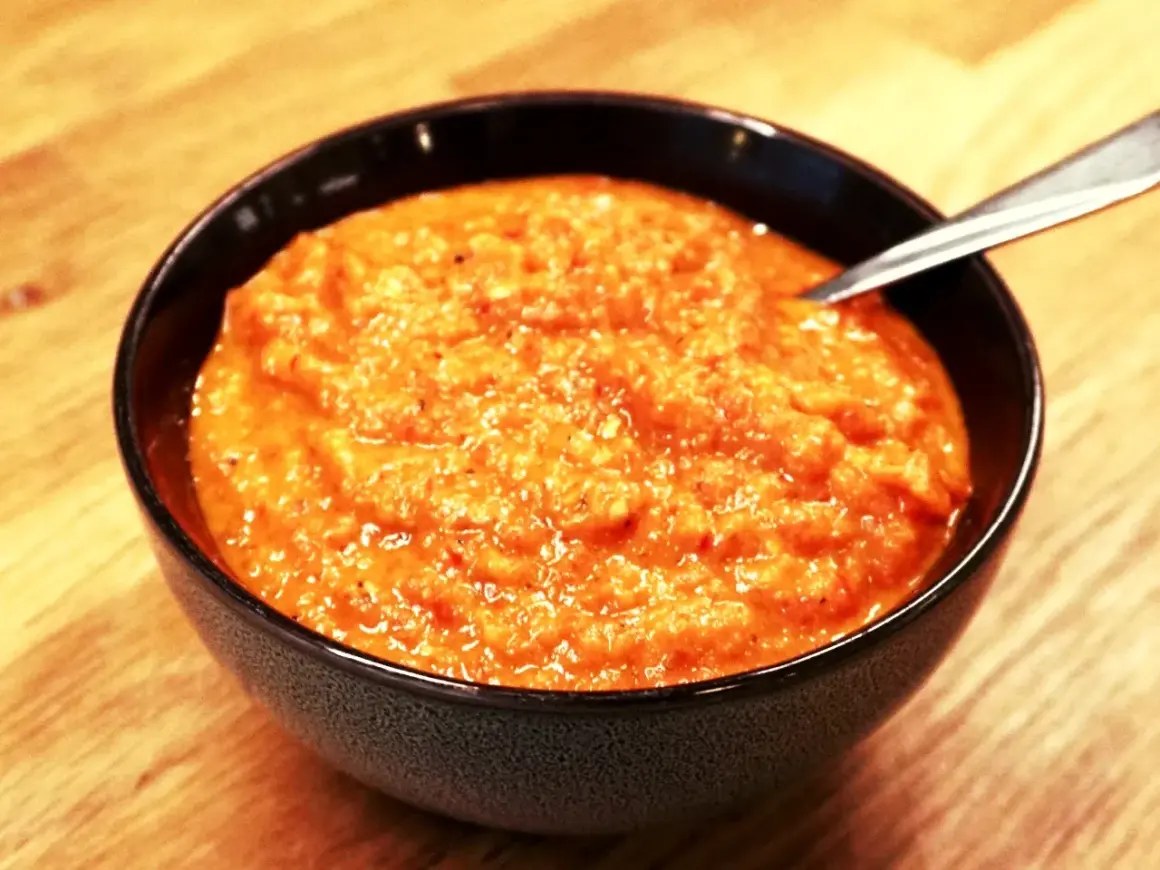 En skål med krämig ajvar, perfekt för ditt ajvar recept. En sked vilar i den orangea röra.
