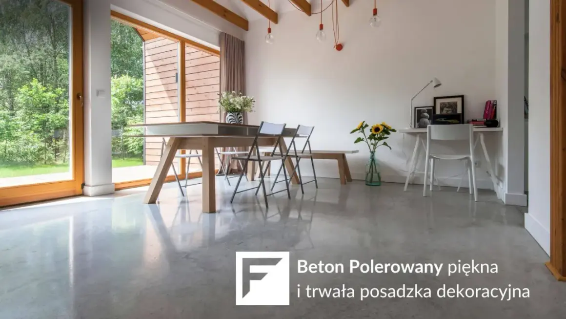 Nowoczesne wnętrze z dużymi oknami i betonem polerowanym na podłodze. W centralnej części stół jadalniany, obok biurko.