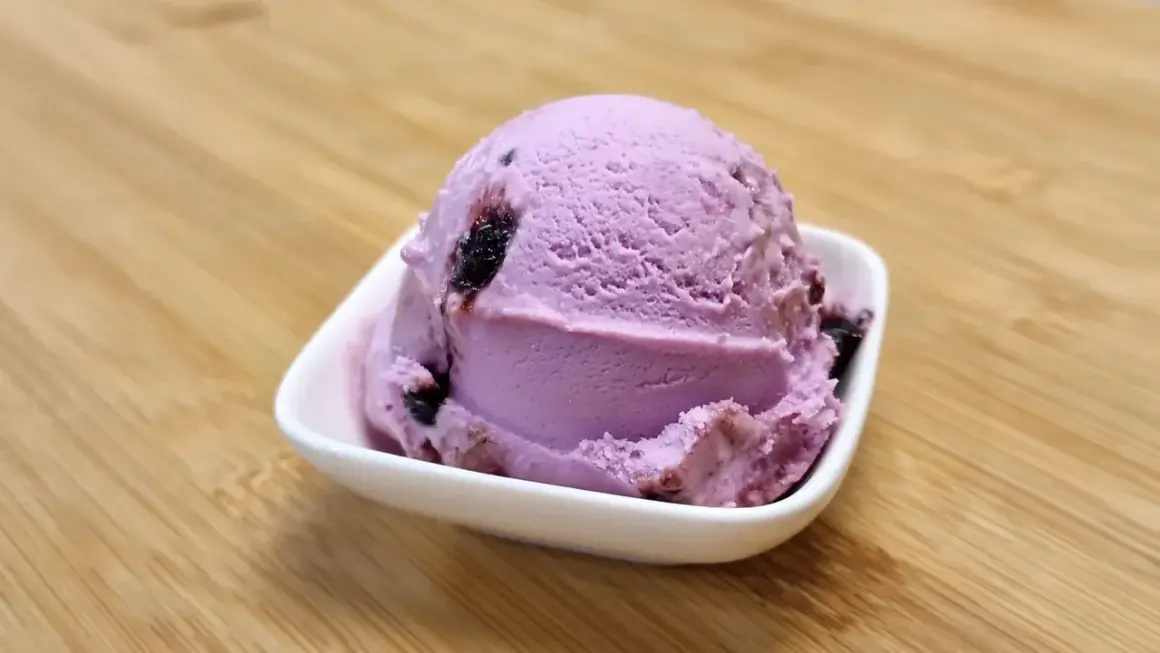 Ein Löffel Amarena-Eis mit Fruchtstückchen, das leicht nach Alkohol duftet, in einer weißen Schale auf Holzuntergrund.