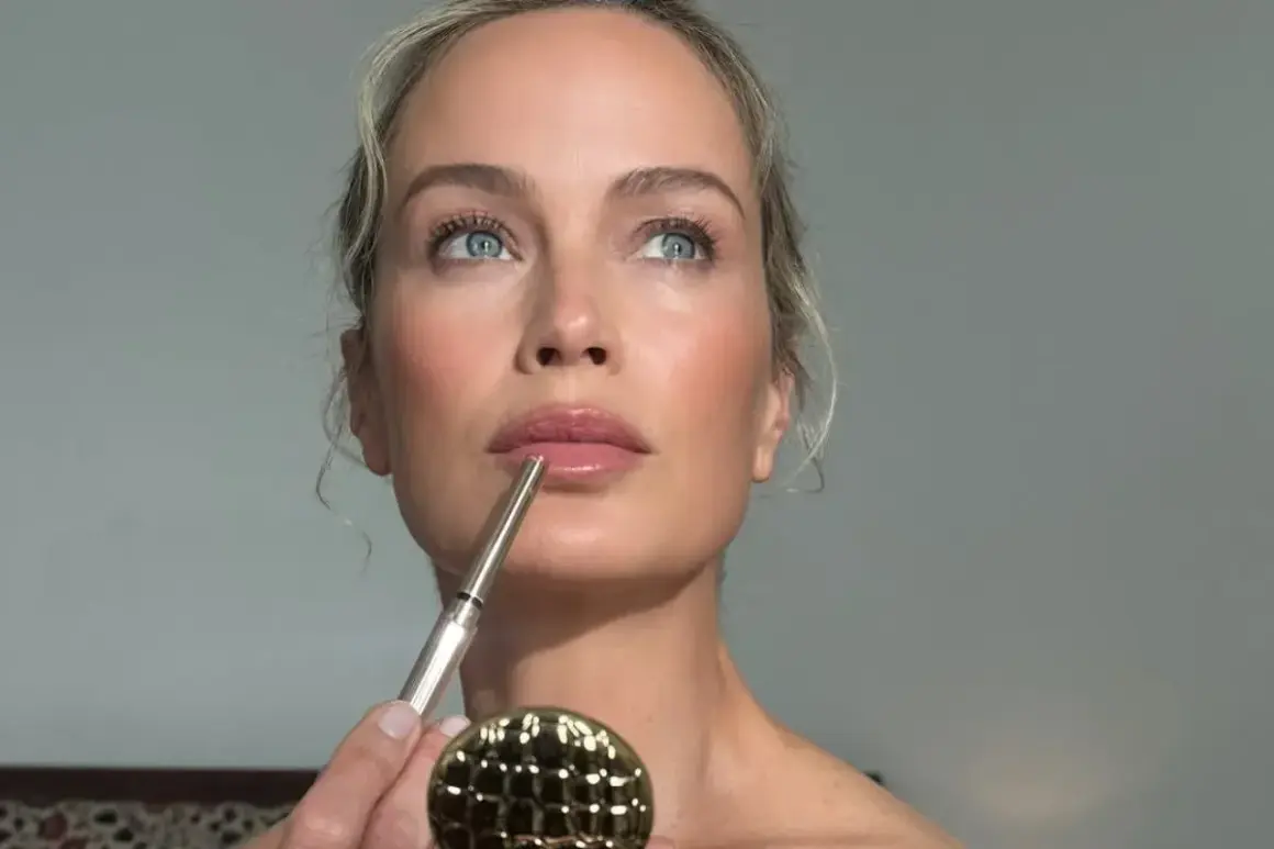 Kobieta z błękitnymi oczami i blond włosami tworzy makijaż glamour, precyzyjnie obrysowując usta konturówką.