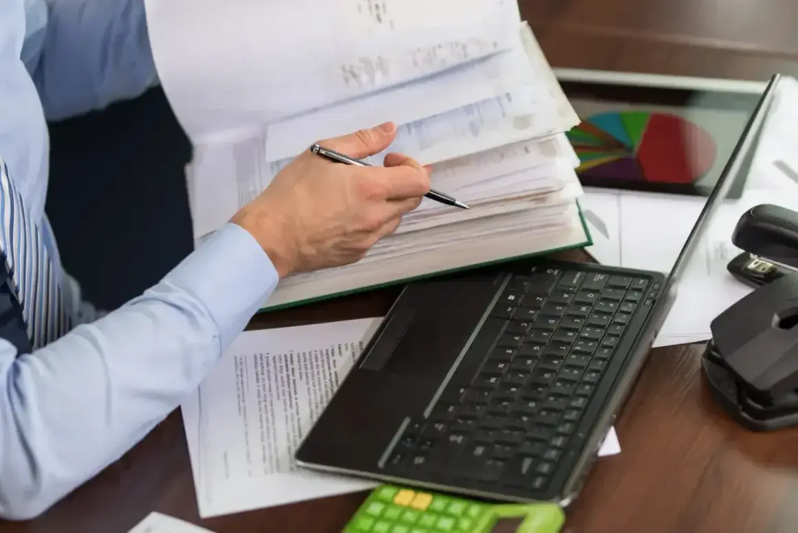 Osoba przegląda dokumenty, na biurku laptop, kalkulator i wykres kołowy. To może być pomocne przy wypełnianiu karty podatkowej.