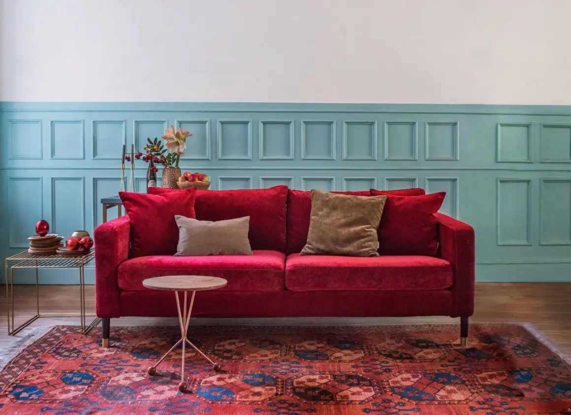 Ein rotes Samtsofa mit braunen Kissen vor einer blau getäfelten Wand. Welche Farbe passt zu Rot? Braun und Blau sind eine tolle Wahl!