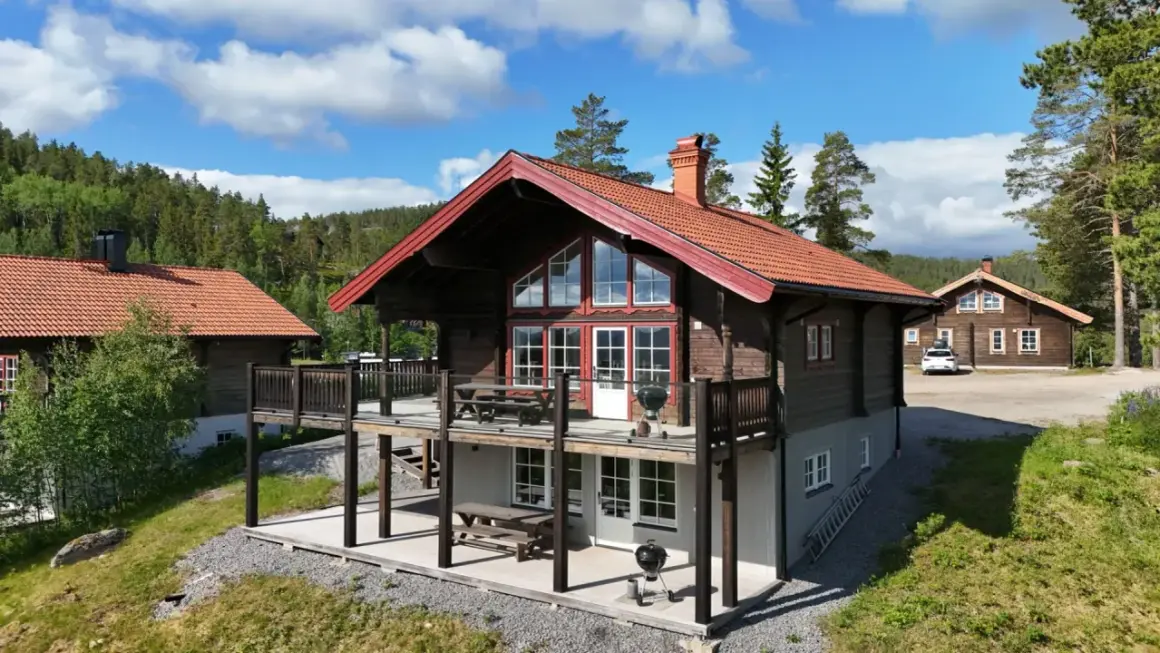 Träfasade hus med röda tak och stora fönster, belägna i en skogsmiljö. En härlig plats att bo på, kanske vid alpstigen i Järvsö.
