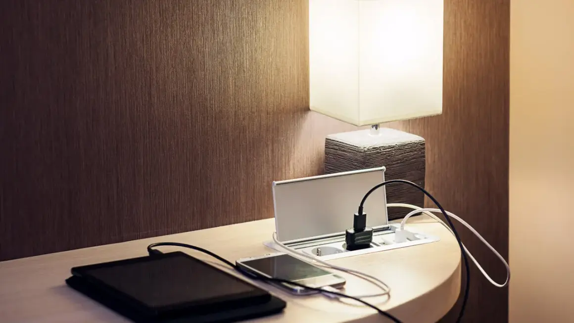 Elegancka ładowarka z gniazdkami i portami USB, idealna do tego, jak ukryć kable. Obok leżą tablet i smartfon.