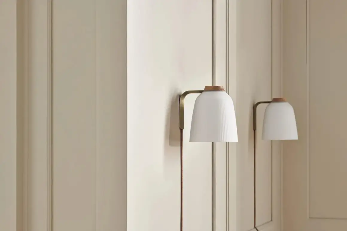 Elegancka lampa klinkiet z białym, plisowanym kloszem i drewnianą nakładką, subtelnie oświetla wnętrze.