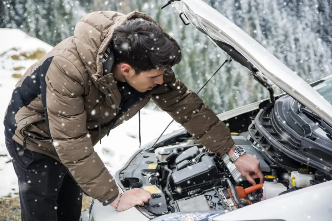 Un homme en doudoune vérifie le moteur de sa voiture sous la neige. Une astuce pour démarrage à froid diesel peut l'aider.