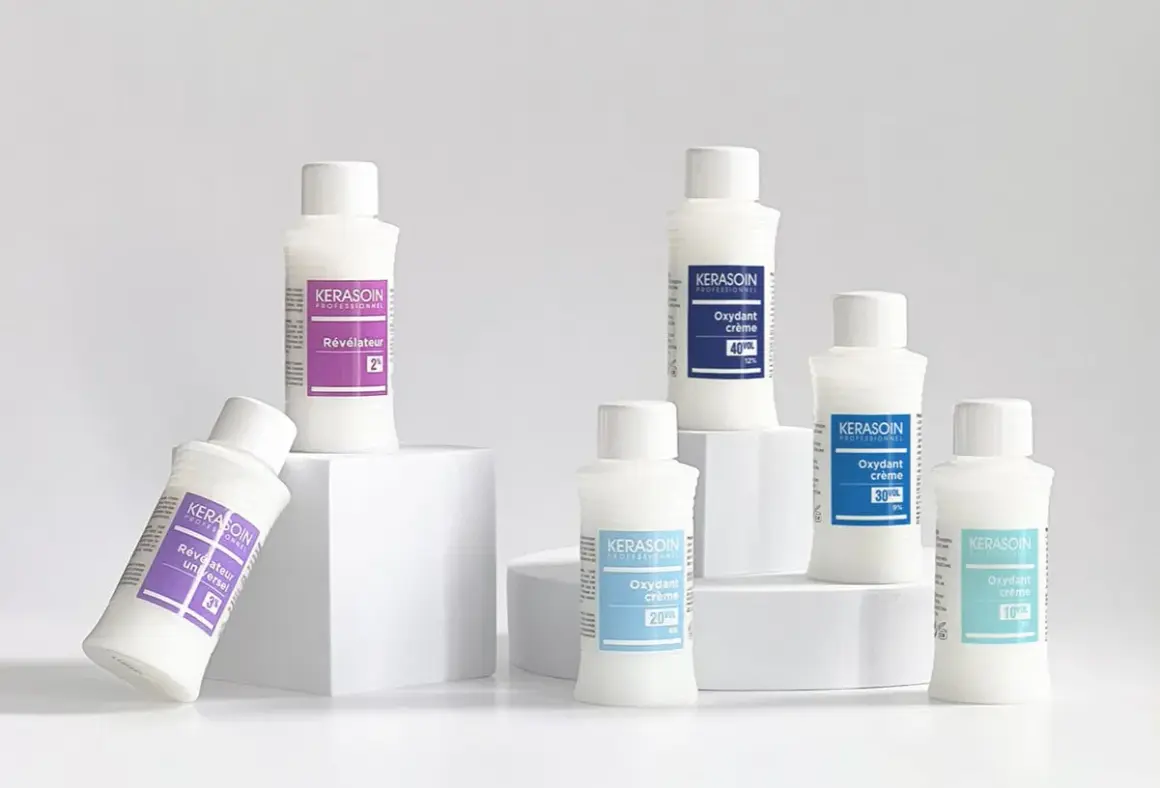 Six bouteilles de produits capillaires Kerasoin, dont un révélateur couleur, disposées sur des cubes blancs.