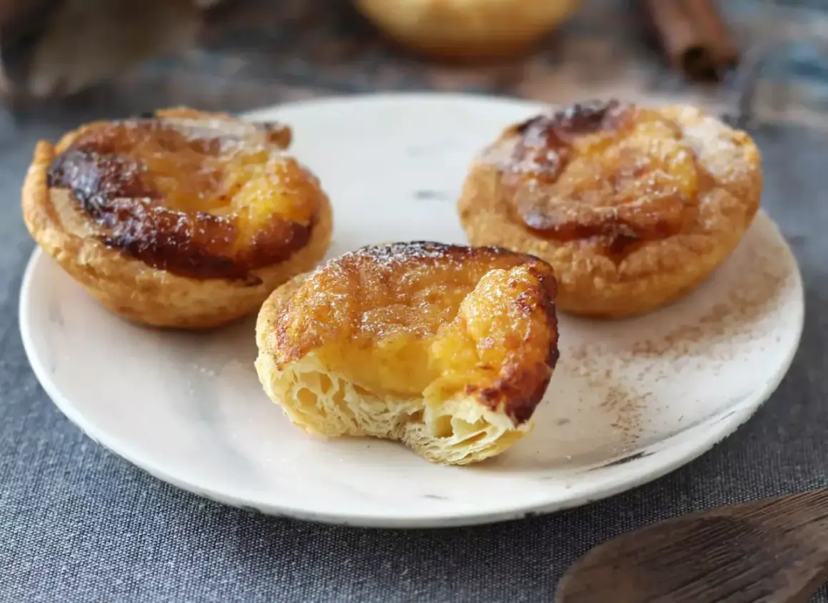 Tre gyllene pastel de nata med krämig fyllning och karamelliserad yta, pudrade med florsocker.