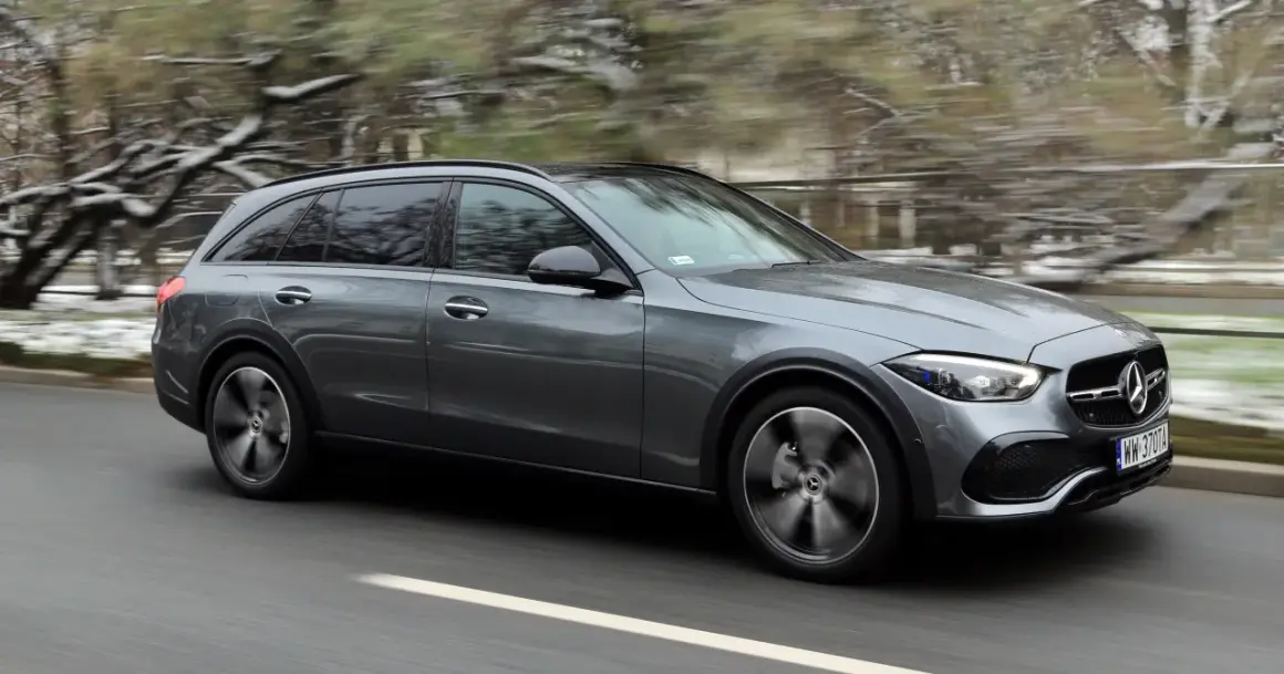 Szary Mercedes All-Terrain z napędem 4matic pędzi po drodze, zaśnieżone drzewa w tle.