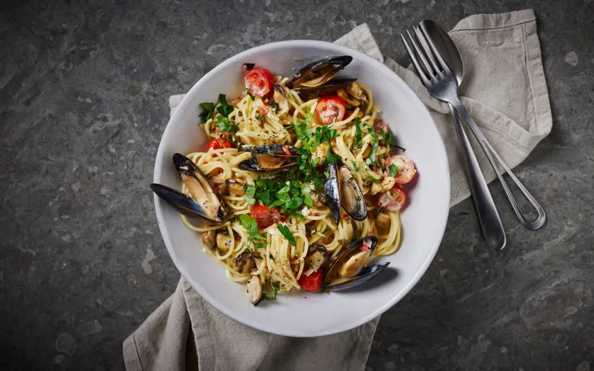 En skål med spaghetti vongole, toppad med färska örter och körsbärstomater. En klassisk italiensk rätt som passar perfekt för en mysig middag.