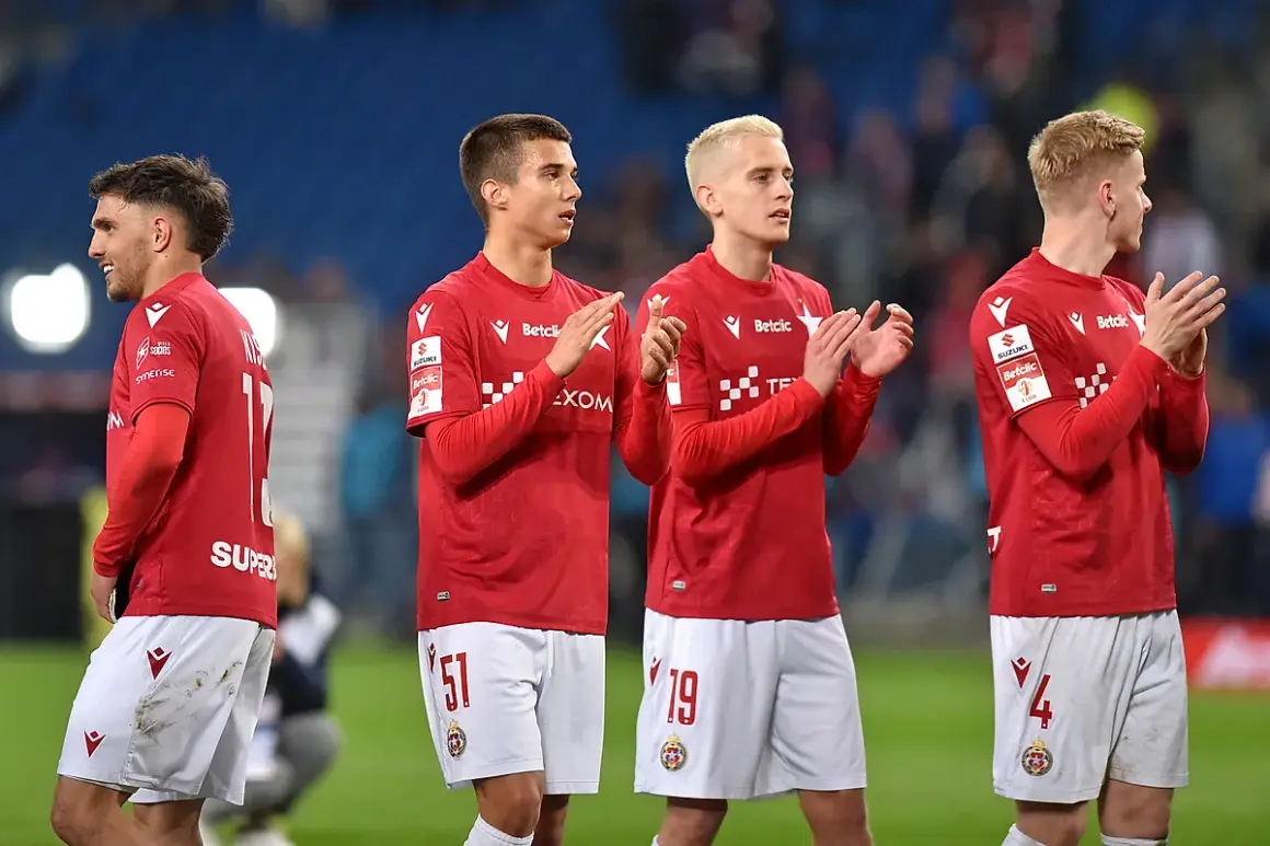 Piłkarze w czerwonych koszulkach i białych spodenkach klaszczą na boisku.