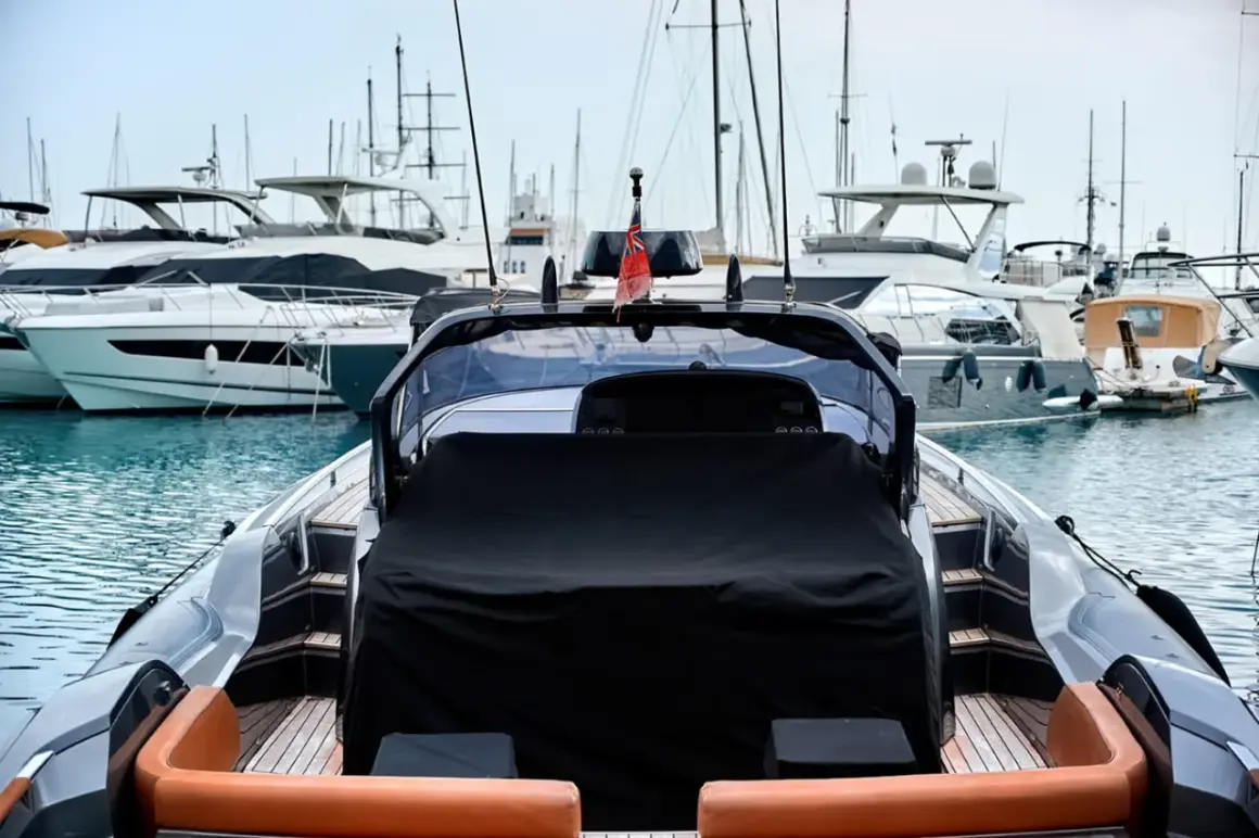 Un porto pieno di yacht di lusso, pronti per il trasporto barche. La vista è dal retro di un gommone con sedili in pelle arancione.