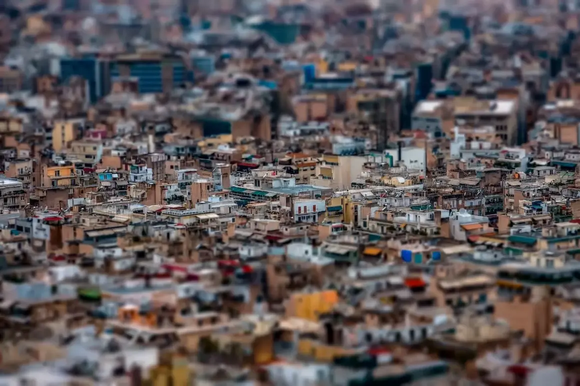 A dense cityscape rendered with tilt shift photography, making the buildings appear like miniature models.