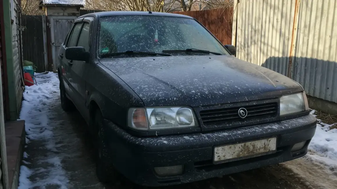 Ciemny samochód pokryty śniegiem i błotem, wyglądający jakby groził mu mandat za brudne auto.