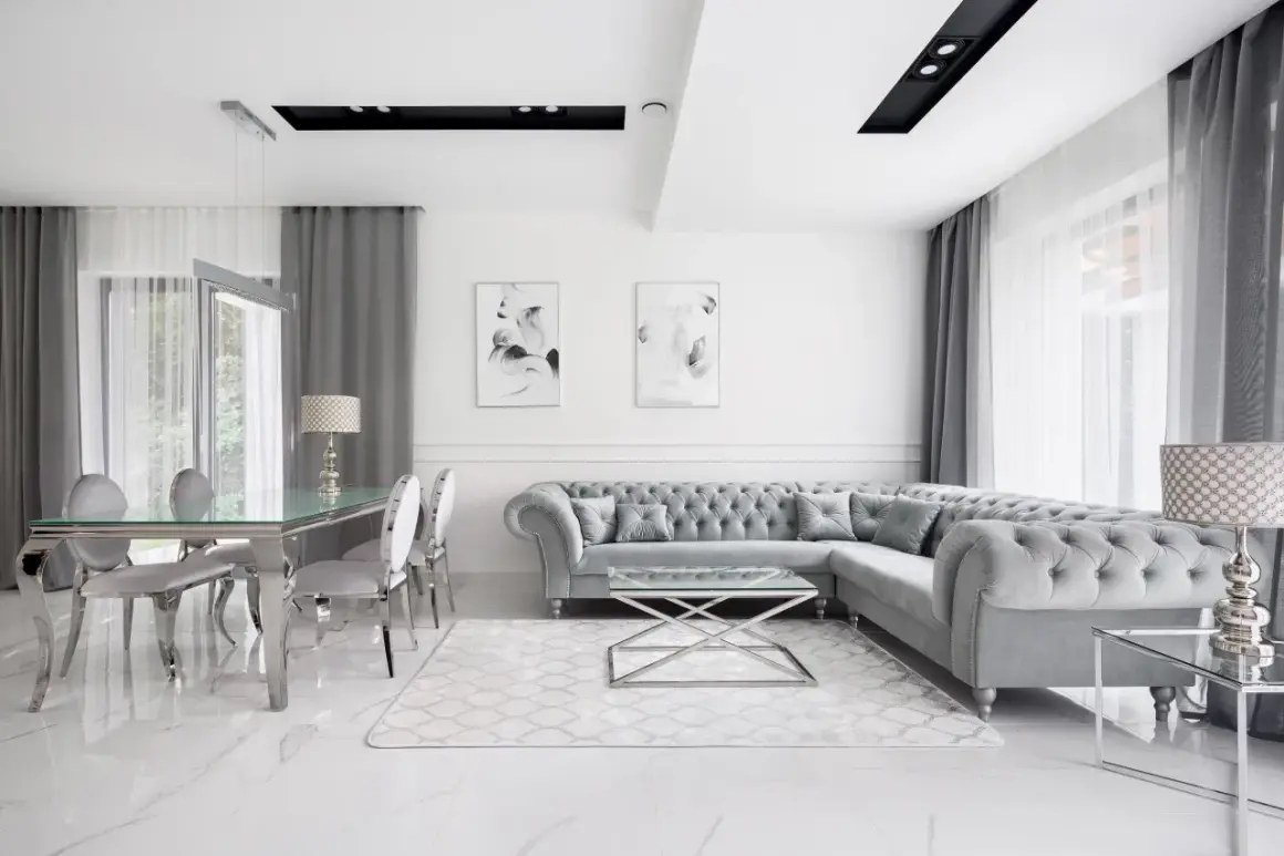 Elegancki salon w stylu nowojorskim z szarą sofą Chesterfield, szklanym stołem i marmurową podłogą.