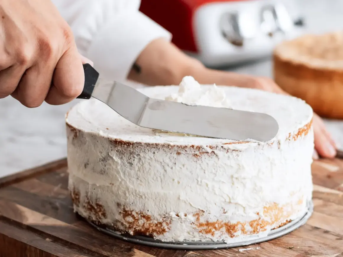 En hand sprider fluffig grädde på en tårta. Ett perfekt tårta recept att följa!